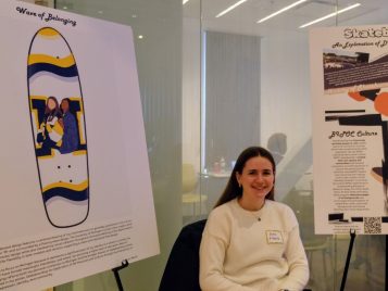 Kathryn Martin sitting beside a poster of her project, "Skateboarding: An Exploration of DIY Practices and Culture."